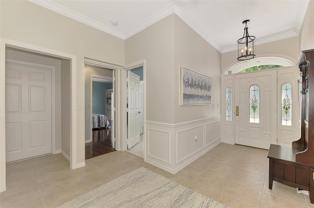 entryway featuring a decorative wall, ornamental molding, wainscoting, light tile patterned flooring, and a chandelier