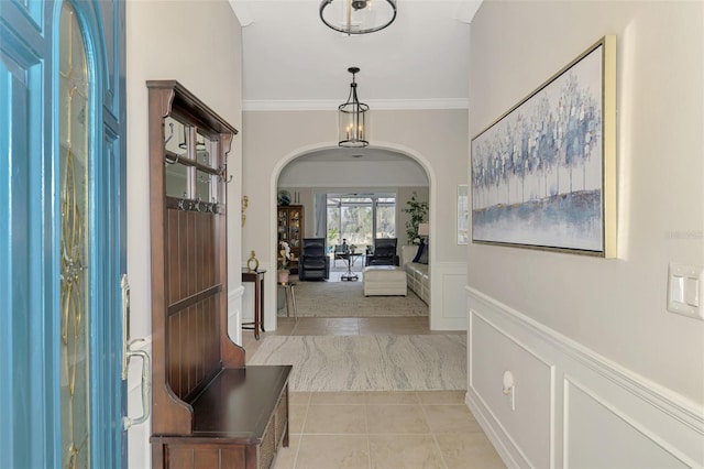 foyer entrance with light tile patterned floors, arched walkways, a wainscoted wall, crown molding, and a decorative wall