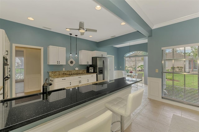 kitchen with a wainscoted wall, a kitchen breakfast bar, white cabinets, stainless steel fridge with ice dispenser, and dark stone counters