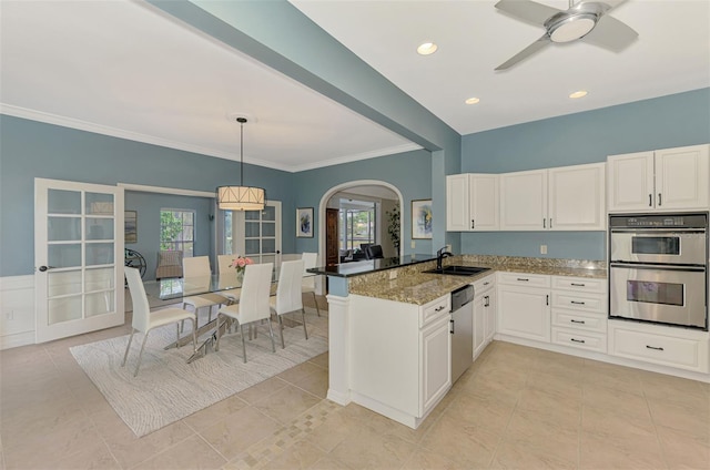 kitchen featuring arched walkways, pendant lighting, appliances with stainless steel finishes, dark stone counters, and a peninsula