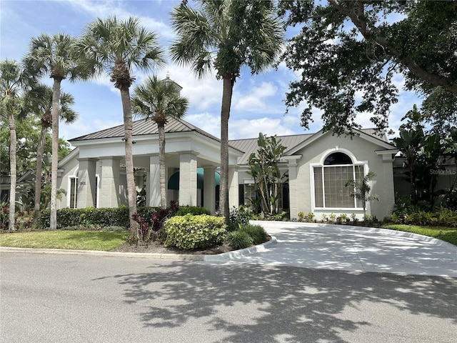 view of front facade featuring metal roof, a standing seam roof, driveway, and stucco siding