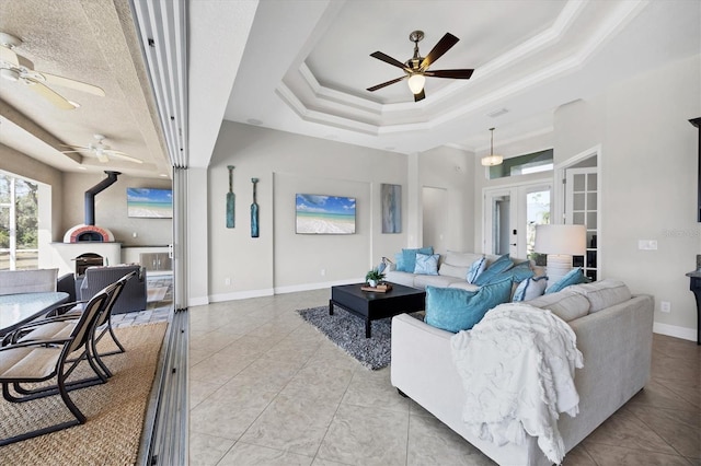 living room featuring a tray ceiling, french doors, ceiling fan, and a wood stove