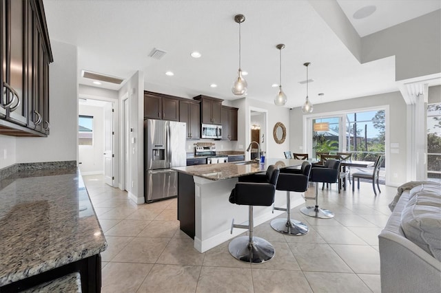 kitchen featuring stone counters, a kitchen island with sink, a sink, hanging light fixtures, and appliances with stainless steel finishes