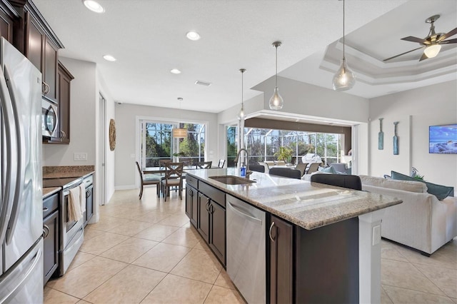 kitchen featuring a kitchen island with sink, stainless steel appliances, a sink, open floor plan, and dark brown cabinets