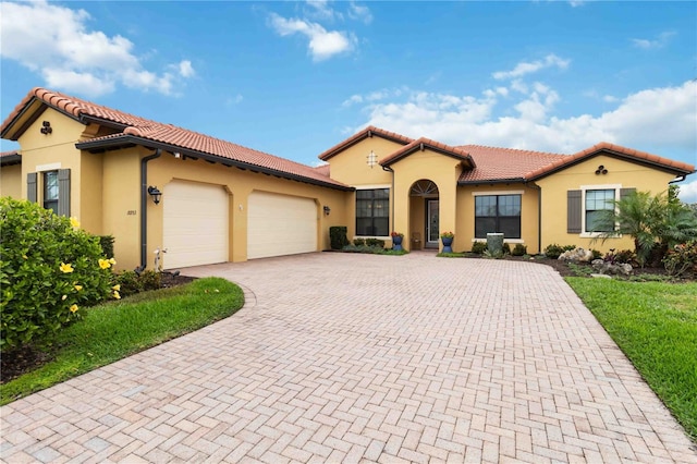 mediterranean / spanish-style home with a garage, stucco siding, decorative driveway, and a tiled roof