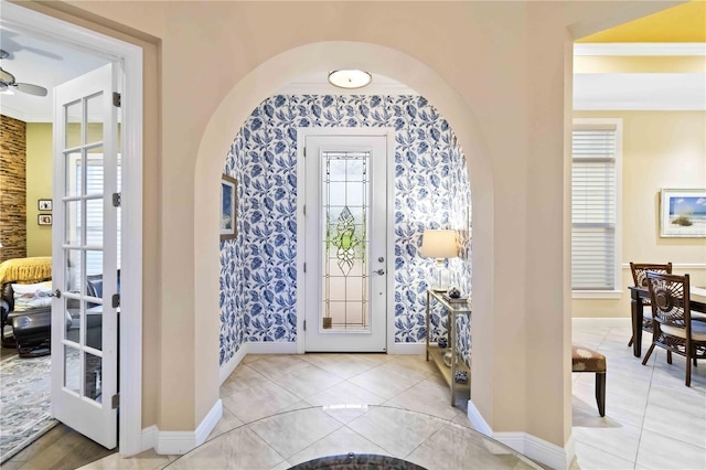 foyer entrance with arched walkways, ornamental molding, light tile patterned flooring, and baseboards