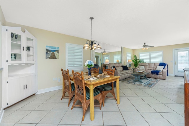 dining area with ceiling fan with notable chandelier, a textured ceiling, baseboards, and light tile patterned floors