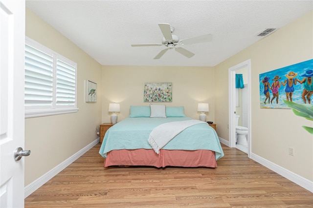 bedroom featuring visible vents, light wood-style flooring, a textured ceiling, ensuite bath, and baseboards