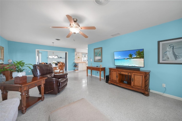 living room featuring ceiling fan with notable chandelier, visible vents, baseboards, and speckled floor