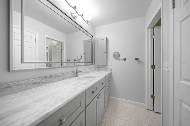 bathroom with a textured ceiling, vanity, baseboards, and speckled floor