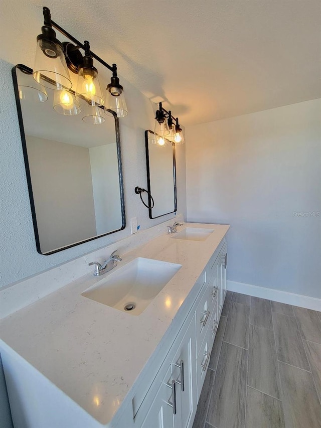 full bath with double vanity, a notable chandelier, baseboards, and a sink