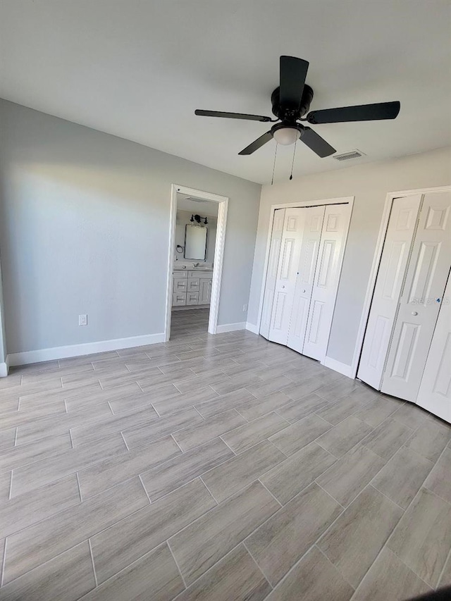 unfurnished bedroom with a ceiling fan, baseboards, visible vents, ensuite bath, and multiple closets