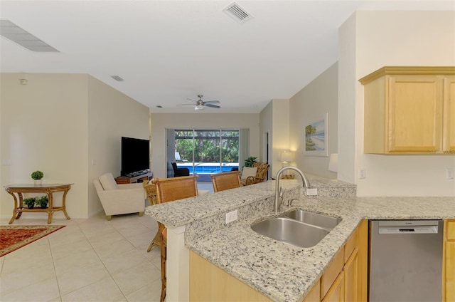 kitchen featuring open floor plan, a peninsula, light brown cabinetry, stainless steel dishwasher, and a sink