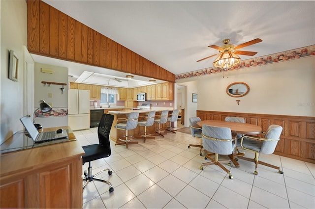 dining area featuring wood walls, light tile patterned floors, vaulted ceiling, and wainscoting