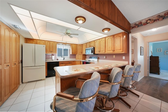 kitchen with light tile patterned floors, a peninsula, white appliances, a kitchen breakfast bar, and light countertops