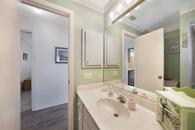 bathroom featuring a textured ceiling, wood finished floors, vanity, visible vents, and baseboards