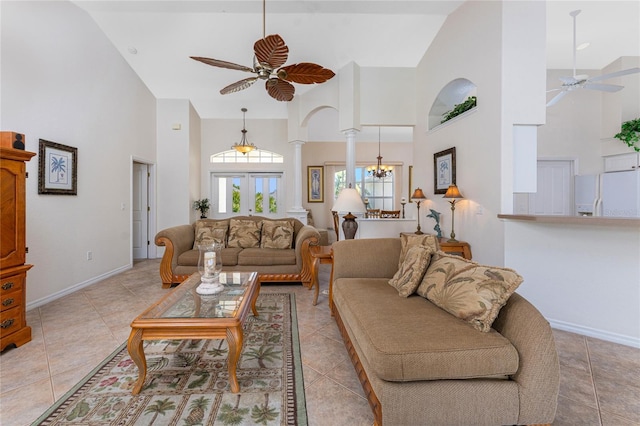 living area featuring light tile patterned floors, decorative columns, baseboards, high vaulted ceiling, and ceiling fan with notable chandelier