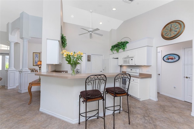 kitchen featuring a peninsula, white appliances, white cabinets, a kitchen bar, and ornate columns