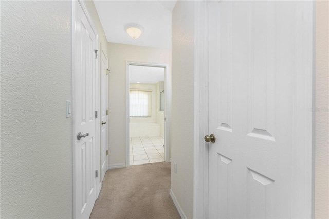 hallway with light colored carpet, a textured wall, and baseboards