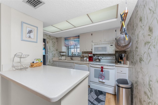 kitchen with a peninsula, white appliances, and light countertops