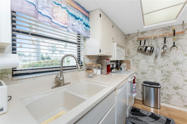 kitchen featuring wallpapered walls, white appliances, white cabinets, light countertops, and a sink
