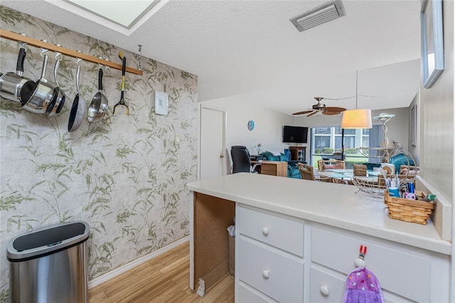 kitchen featuring light countertops, visible vents, white cabinets, light wood-type flooring, and wallpapered walls