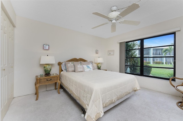 bedroom featuring a textured ceiling, ceiling fan, a closet, and light colored carpet