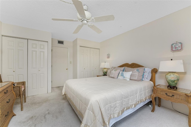bedroom with multiple closets, visible vents, light carpet, and a textured ceiling