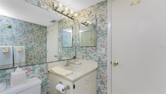 bathroom with visible vents, vanity, toilet, and wallpapered walls