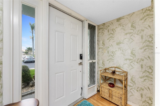interior space featuring wood finished floors, a textured ceiling, and wallpapered walls