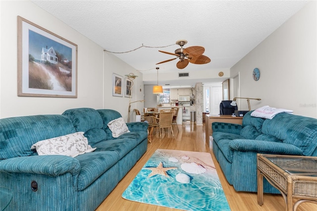 living room with a ceiling fan, a textured ceiling, and light wood finished floors