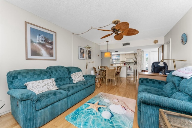 living room featuring light wood finished floors, a ceiling fan, visible vents, and a textured ceiling