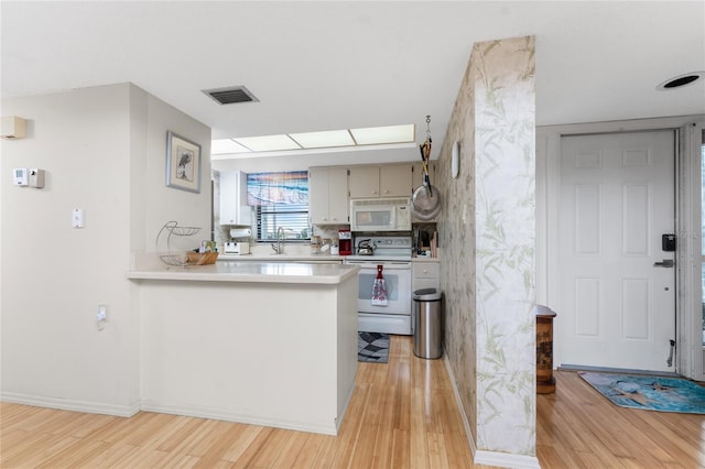 kitchen featuring white appliances, light wood finished floors, visible vents, a peninsula, and light countertops