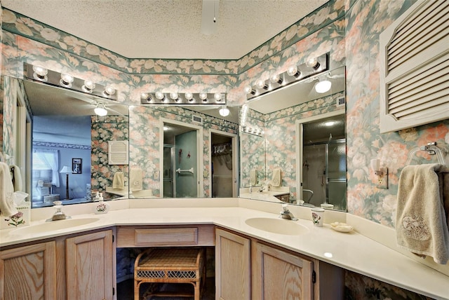 bathroom featuring a sink, a textured ceiling, a shower stall, and wallpapered walls