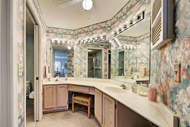 full bathroom with double vanity, wallpapered walls, a ceiling fan, a textured ceiling, and a sink