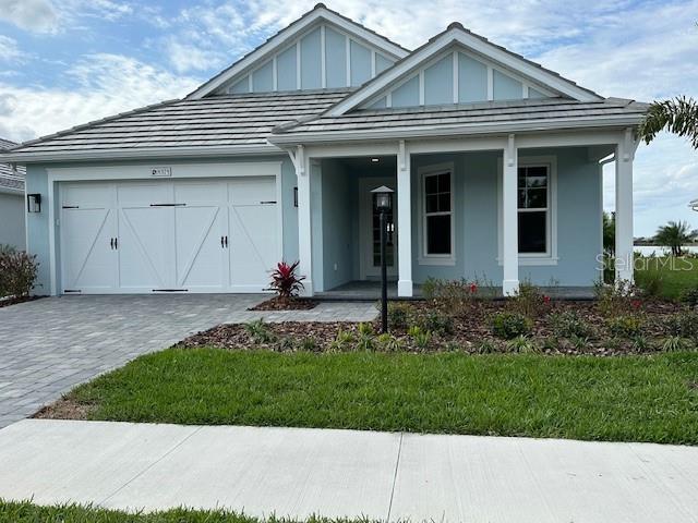 view of front facade featuring decorative driveway, covered porch, an attached garage, board and batten siding, and a front yard