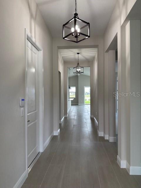 hallway featuring baseboards and a notable chandelier