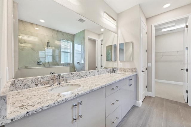 full bath with a spacious closet, a tile shower, a sink, and wood finished floors