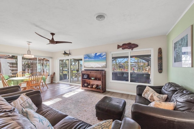 living area featuring a textured ceiling, a ceiling fan, visible vents, baseboards, and light wood finished floors