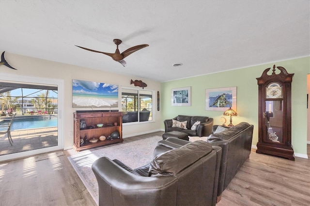 living room with light wood-style floors, a sunroom, ceiling fan, and baseboards