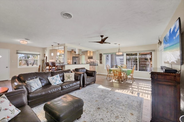 living room with a ceiling fan, baseboards, visible vents, and wood finished floors