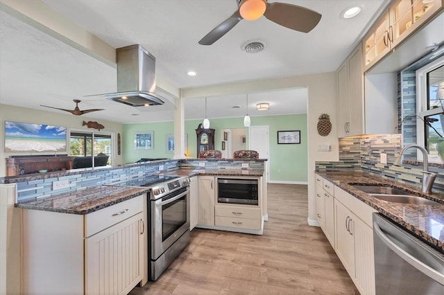 kitchen featuring pendant lighting, stainless steel appliances, a sink, island range hood, and a peninsula