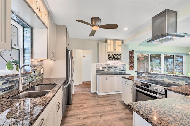 kitchen with island range hood, glass insert cabinets, a sink, light wood-type flooring, and backsplash