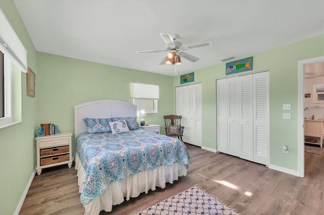 bedroom with baseboards, visible vents, multiple closets, and wood finished floors