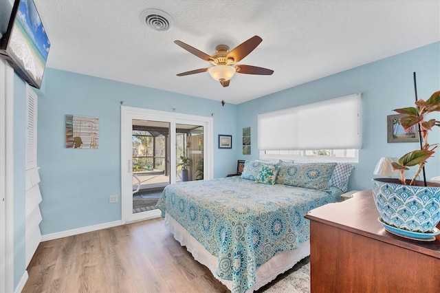 bedroom featuring a textured ceiling, wood finished floors, visible vents, baseboards, and access to outside