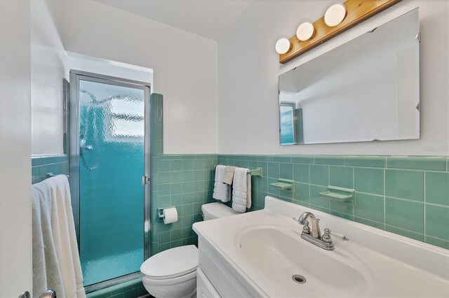 full bathroom featuring tile walls, toilet, a stall shower, wainscoting, and vanity