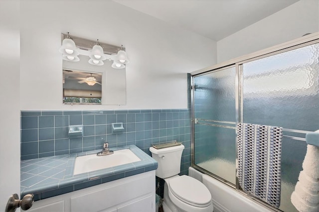 full bathroom with toilet, vanity, tile walls, combined bath / shower with glass door, and wainscoting