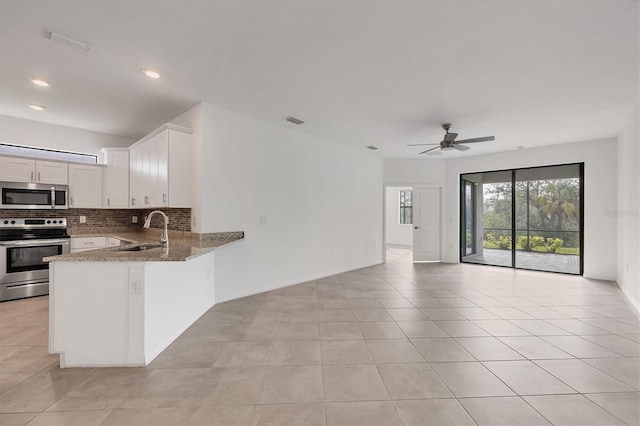 kitchen featuring light stone counters, decorative backsplash, appliances with stainless steel finishes, open floor plan, and a sink