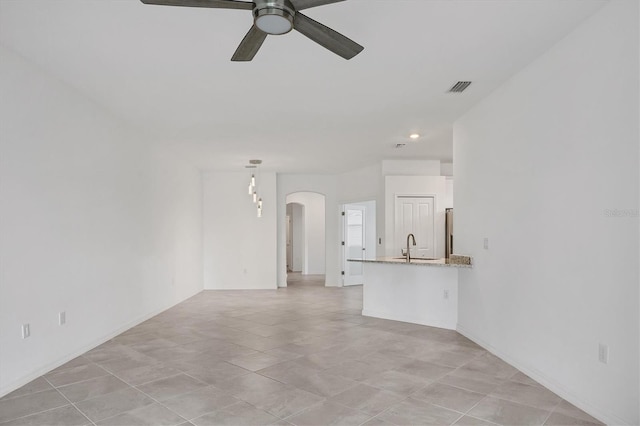 unfurnished living room featuring a ceiling fan, arched walkways, visible vents, and a sink