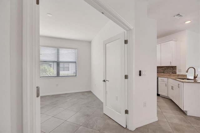 corridor featuring light tile patterned floors, baseboards, visible vents, and a sink